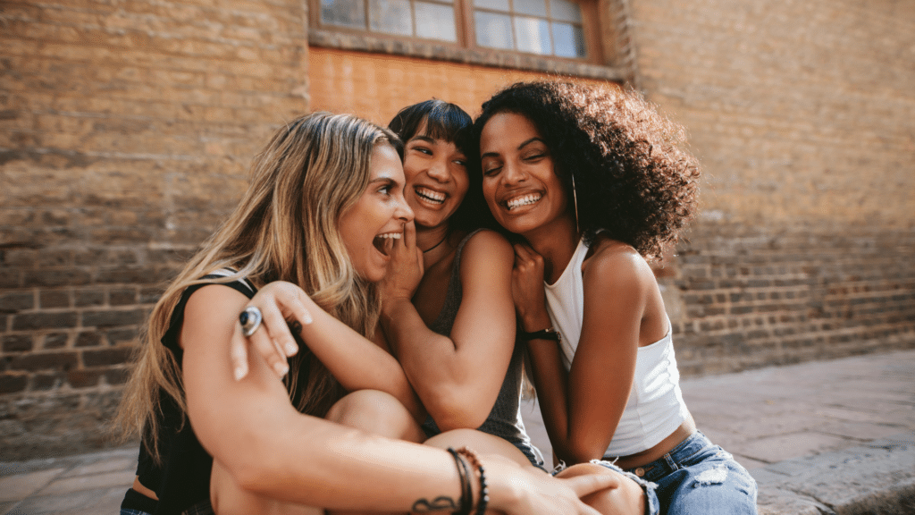 Trois jeunes femmes souriantes et complices se serrant dans les bras, illustration de l'esprit de communauté et d'amitié au 20/80 Fit Club de Sallanches