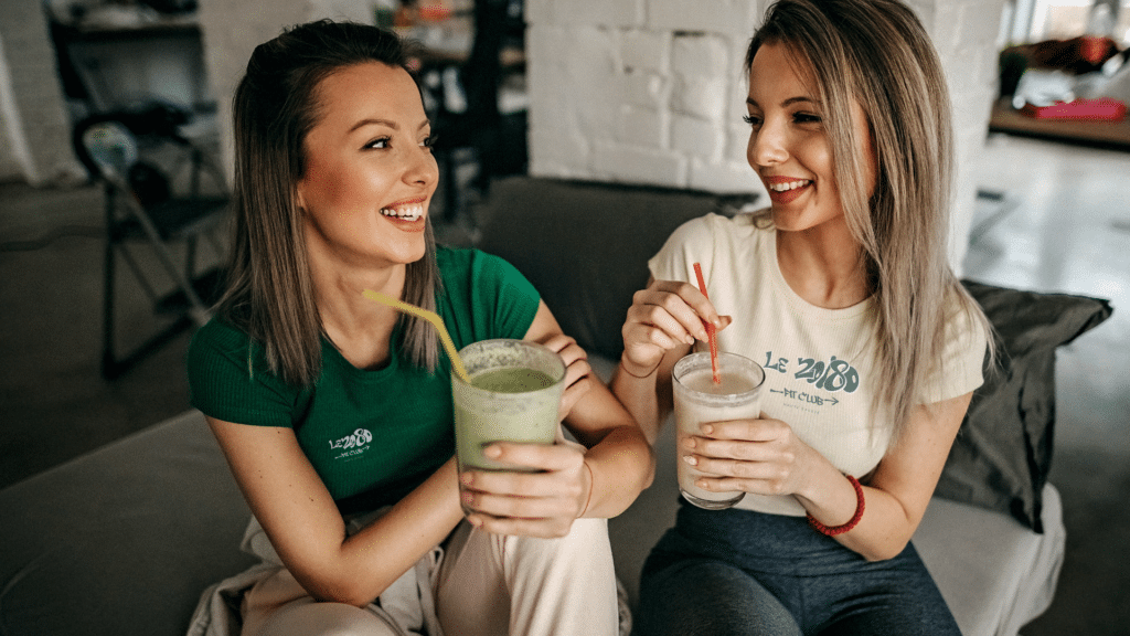 Deux membres du 20/80 Fit Club de Sallanches souriantes dégustant des smoothies après leur entraînement, portant les t-shirts officiels du club