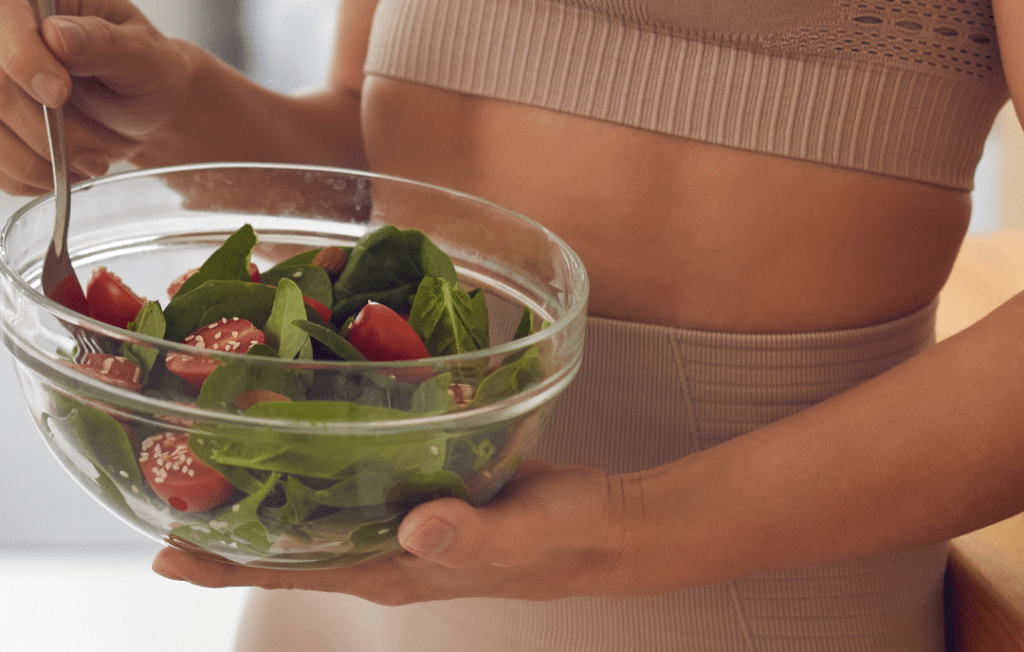 Femme en tenue de sport tenant un saladier de salade fraîche et équilibrée