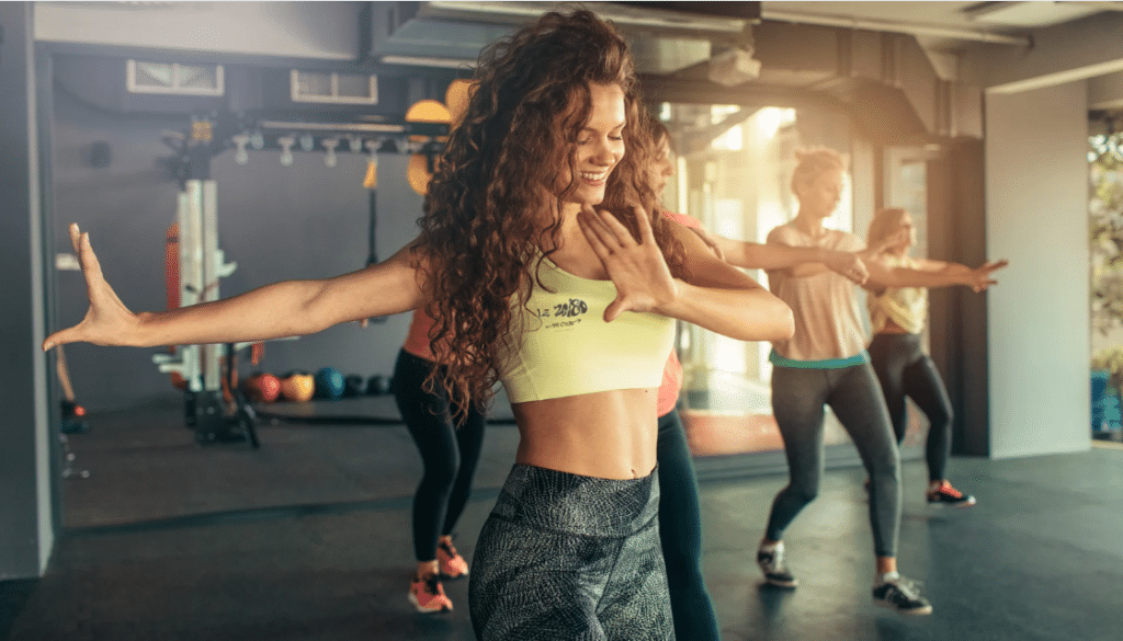 Cours de fitness collectif en salle avec une coach souriante