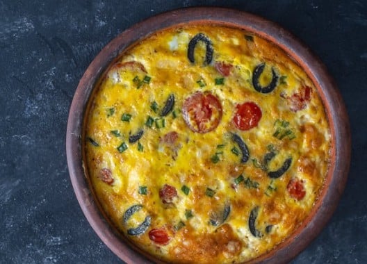 Omelette aux légumes avec tomates cerises, courgettes, champignons et ciboulette dans un plat en terre cuite
