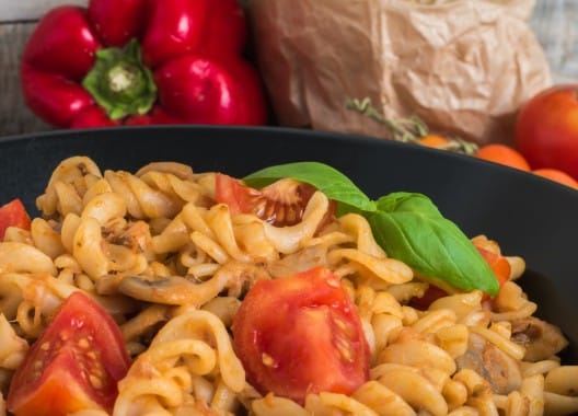 Pâtes complètes au thon avec tomates cerises, champignons et basilic frais dans un plat noir lors d'un atelier cuisine