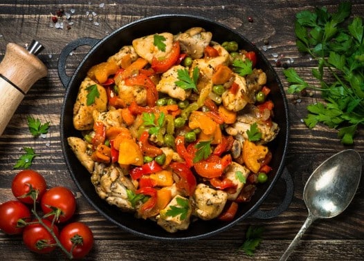 Poêlée de poulet aux légumes croquants avec poivrons, carottes, petits pois et persil frais dans une poêle en fonte