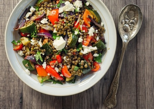 Salade de lentilles vertes avec feta émiettée, poivrons rouges, courgettes et oignon rouge dans une assiette blanche lors d'un atelier cuisine