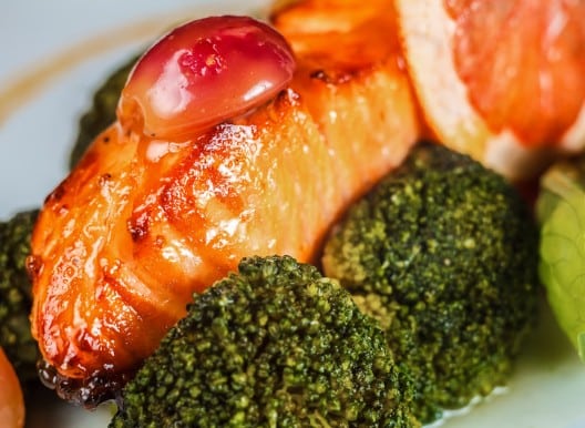 Filet de saumon poêlé glacé avec brocolis vapeur et tomate cerise sur assiette blanche