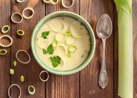 Velouté de poireaux et pomme de terre onctueux dans un bol vert avec rondelles de poireau et persil frais