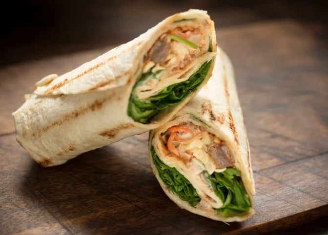 Wrap poulet avocat coupé en deux avec roquette, légumes et tortilla complète sur une planche en bois lors d'un atelier cuisine